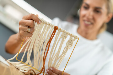 Weaving tapestry at home as an artistic  hobby. Smiling woman, satisfied with her progress, checking the tapestry loom