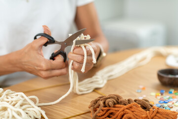 Woman preparing tapestry materials by cutting rope at home. Highlights precision, hand control, and structured textile craft technique.