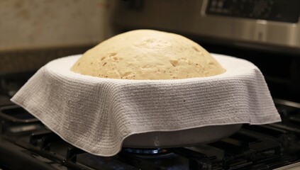 Bread dough rising with towel on stove top