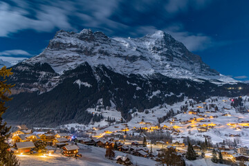 The famous Swiss Als peak Eiger Mountain and the wonderland village Grindelwald at its foot in a moonlit winter night.