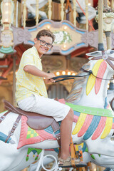 A young boy is riding a carousel horse with a smile on his face. The carousel is decorated with colorful feathers and lights, creating a fun and playful atmosphere