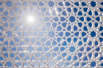 A detailed view of a white geometric design against a blue sky, showcasing intricate patterns and the effect of sunlight shining through.