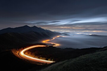 Curving road illuminated at night, mountains, fog, city lights below