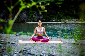 Young Japanese woman meditating in lotus pose during outdoor yoga by a river, calm sustainable lifestyle concept with mindfulness and mental wellbeing
