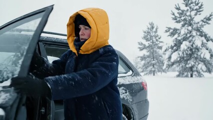 Womans legs in blue coat and black boots standing in snow next to black suv on cold winter day outside