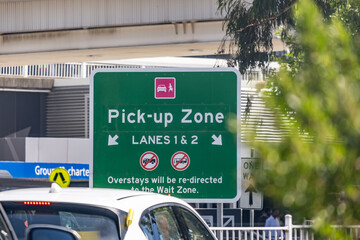 A roadside sign marks the Pick-up Zone at Melbourne Airport, Australia, directing vehicles to designated lanes for passenger collection. Ground transport management, vehicle flow control