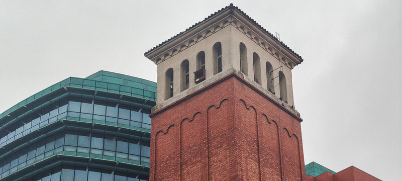 Torre de ladrillo de estilo cl&aacute;sico con arcos frente a edificio de oficinas moderno bajo cielo nublado, en Burgos, Espa&ntilde;a