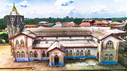Aerial view of a grand, weathered church with a towering steeple, its aged facade a tapestry of fading colors against the lush greenery, Abonnema, Port Harcourt, Nigeria.