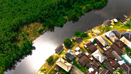 Aerial view of the winding river reflecting sunlight alongside dense green forests and clustered rooftops, Abonnema, Port Harcourt, Nigeria.