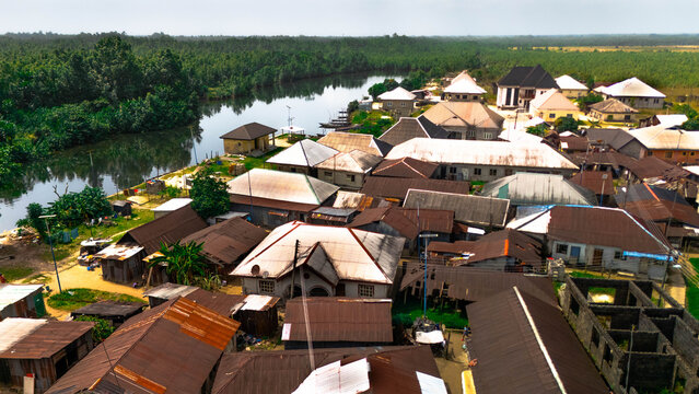 Aerial view of a vibrant community nestled along a winding river, the metallic roofs contrasting with the lush green trees, Abonnema, Port Harcourt, Nigeria.