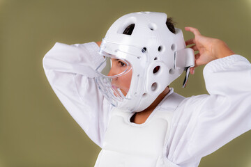 Boy in karate outfit, wearing karate gear, adjusting protective helmet onto head. Highlights careful preparation, focus, and controlled martial arts routine.