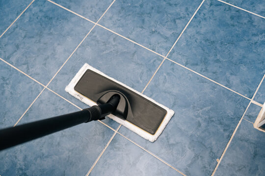 High-angle view of steam cleaner sanitizing blue tiled bathroom floor, releasing steam for deep cleaning and hygiene, maintaining fresh and disinfected home environment. Concept of household chores.