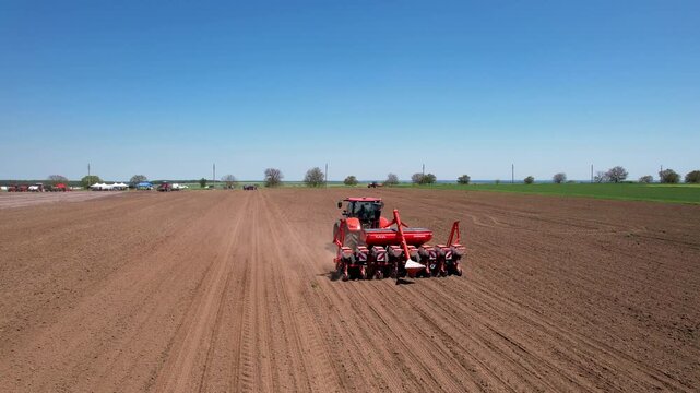 Aerial view of a red tractor meticulously plowing the rich, brown soil, creating linear patterns under a clear blue sky, Silistra, Bulgaria.