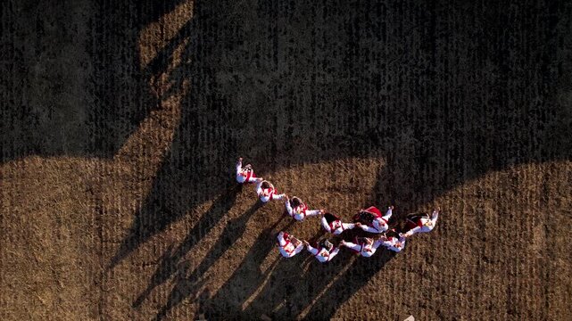 Aerial view of people in traditional clothing forming a circle, casting long shadows on the textured ground, creating a vibrant and striking visual, Silistra, Bulgaria.