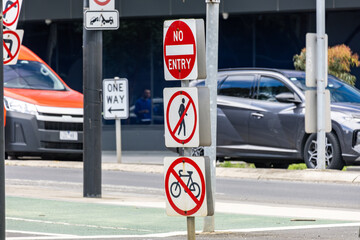 A cluster of road and traffic restriction signs mounted on a pole in an urban street in Melbourne CBD, Australia, including no entry, no pedestrians, and no bicycles symbols. Road safety regulation