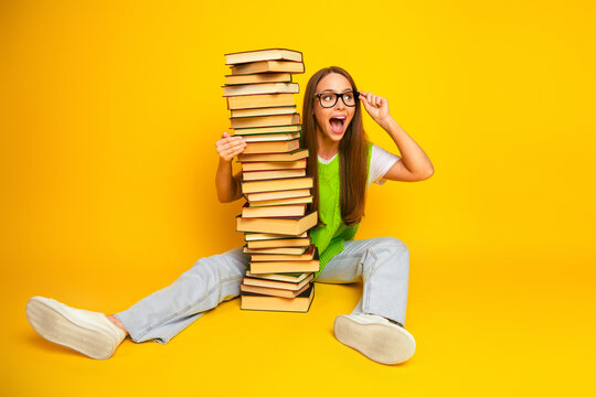 Young woman student with a tall stack of book smiling against a bright yellow background for education lifestyle stock photo - Powered by Adobe