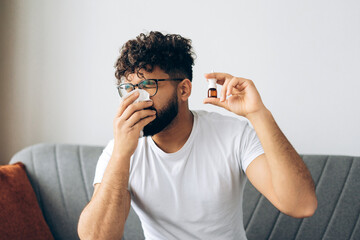 Sick, sad man blowing nose with tissue holding nasal spray sitting at home, treatment