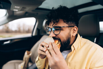 Middle eastern man eating fast food burger in car