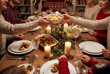 Family passing bowl of food across festive holiday dinner table