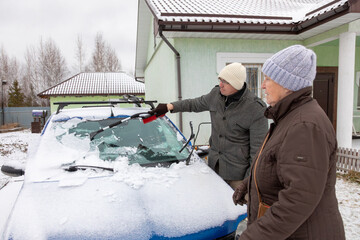 Elderly woman with her son removing snow from a car. Winter weather challenges and senior support in colder climates.