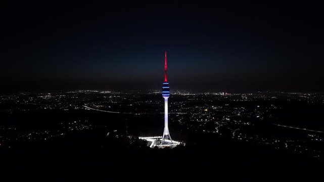 Aerial view of the Avala Tower illuminated against the dark night sky, standing tall above the city lights creating a stark contrast, Belgrade, City of Belgrade, Serbia.