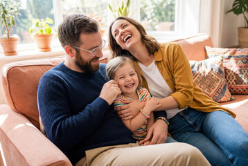 Smiling mother and father enjoying a joyful moment with their young daughter while sitting on a cozy living room couch.