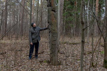 A man in a forest admires an ancient wooden sculpture, observing the detailed carvings on the totem pole. Outdoor adventure and cultural exploration in nature.