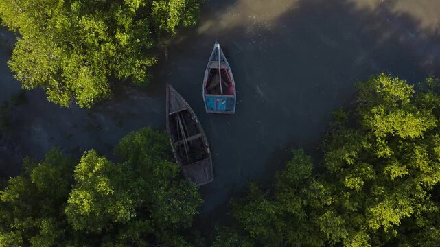 Aerial view of two rustic boats moored in shallow water surrounded by lush green trees, reflecting the sunlight, Maputo, Cidade de Maputo, Mozambique.