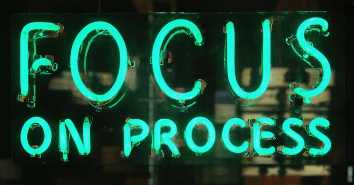 Bright neon sign displays text. Words focus on process glow vividly against dark background. Simple, motivational message.