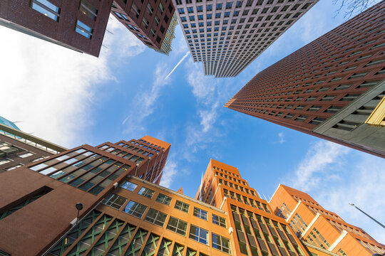 View of red and pink brick buildings reaching up to a blue sky with scattered clouds from a low-angle perspective, The Hague, South Holland, Netherlands.