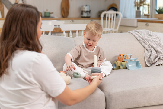 Happy family at home. Mother and baby boy playing with toys in couch at home indoors. Little toddler child and babysitter nanny having fun together. Young woman mom kid son rest in living room