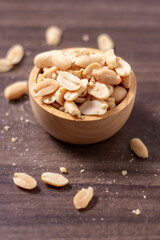 Peanuts in a wooden cup rest on a natural wood floor, creating a warm and rustic food-themed scene.