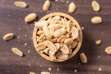 Peanuts in a wooden cup rest on a natural wood floor, creating a warm and rustic food-themed scene.
