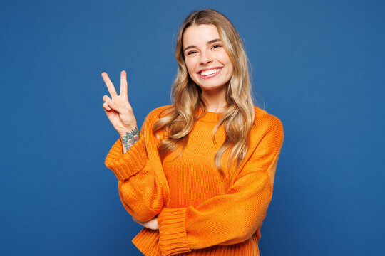 Young happy cheerful smiling student fun Caucasian woman she wear yellow sweater casual clothes showing victory sign look camera isolated on plain blue background studio portrait. Lifestyle concept.