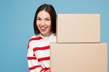 Young smiling woman she wear red striped sweatshirt casual clothes hold stack of two blank cardboard boxes look camera isolated on plain pastel light blue background studio portrait Lifestyle concept