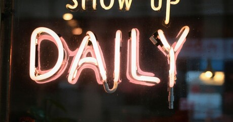 Bright neon sign displays DAILY. Raindrops cover glass surface. Dark background creates strong contrast, emphasizing glowing text.