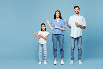 Full body young happy parents mom dad with child kid daughter girl wearing casual clothes point index finger aside on blank empty area isolated on plain blue background. Family day childhood concept.