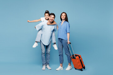 Traveler young fun parents mom dad child wear casual clothes hold suitcase bag isolated on plain blue background. Tourist travel abroad in free spare time rest getaway Air flight trip journey concept © ViDi Studio