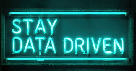 Obraz premium Bright neon sign displays text Stay Data Driven. Dark background emphasizes glowing turquoise illumination. Simple rectangular frame surrounds message.