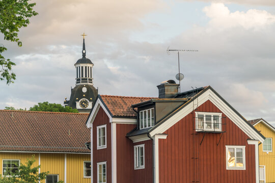 View of colorful wooden houses and the steeple of the Vastervik Church under a cloudy sky, creating a charming scene, Vastervik, Kalmar County, Sweden.