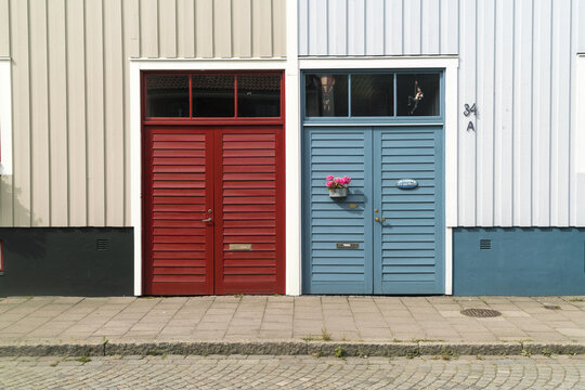 View of vibrant red and blue doors stand side-by-side on quaint buildings, their colors popping against the neutral facades, reflecting the charm, Vastervik, Kalmar County, Sweden.