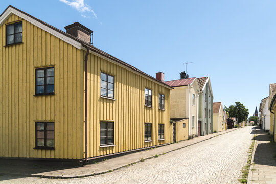 View of a quaint street lined with colorful wooden houses under a bright blue sky, offering a glimpse into classic Swedish architecture, Vastervik, Kalmar County, Sweden.