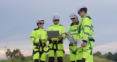 Caucasian engineer group analyzing renewable energy data using laptop and blueprint near wind turbine, teamwork collaboration managing sustainable power project field inspection under cloudy sky - Powered by Adobe