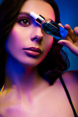 Close-up vertical photo of glamorous woman holding skincare serum in vibrant colored lights,...