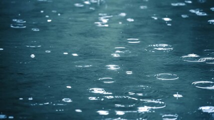Raindrops hitting dark water surface creating ripples and splashes
