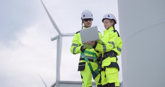 Engineer team reviewing maintenance results on laptop near wind turbine, professional workers ensuring renewable energy performance, teamwork representing innovation, and green technology progress