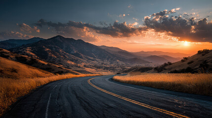 Winding road through golden fields leading to mountains at dramatic sunset with vibrant sky
