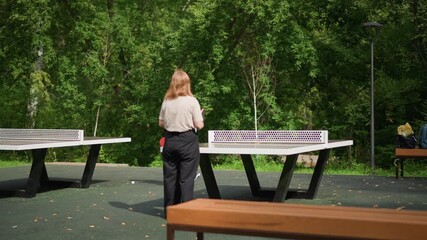 Redhaired Woman Guides Young Player, Outdoor Scene Of Woman Instructing Boy In Tennis Techniques, Green Park Setting With Woman Teaching Young Boy Tennis Skills At Table Tennis Station