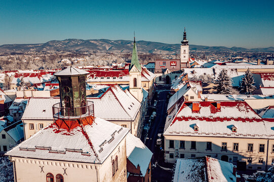 Aerial view of snow-dusted rooftops and the iconic spires of Zagreb's churches pierce the crisp winter air, framed by distant, snow-capped mountains, Zagreb, Croatia.