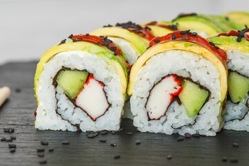 Sushi rolls with imitation crab and cucumber, topped with slices of avocado and drizzled with sauce.
